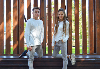 A young girl and a young man in the same clothes sitting on a wooden bench.