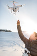 © lightpoet - Young man controlling his drone in snowy outdoors. Drone operator holding a transmitter and landing with a drone.