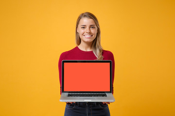 Smiling young blonde woman girl in casual clothes posing isolated on yellow orange background in studio. People lifestyle concept. Mock up copy space. Hold laptop pc computer with blank empty screen.