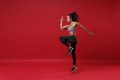 © ViDi Studio - Side view of young african american fitness woman in sportswear posing working out isolated on red wall background studio portrait. Sport exercises healthy lifestyle concept. Jumping like running.