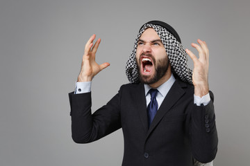 Angry bearded arabian muslim businessman in keffiyeh kafiya ring igal agal classic black suit shirt isolated on gray background. Achievement career wealth business concept. Swearing spreading hands.