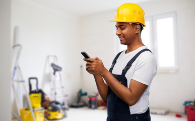 Poster - profession, construction and building - happy smiling indian worker or builder in helmet using smartphone over room with working equipment at new home or apartment background