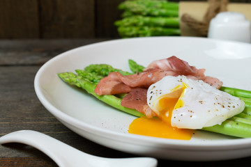 Asparagus in oyster sauce with onsen egg and bacon in white dish on wooden table background.