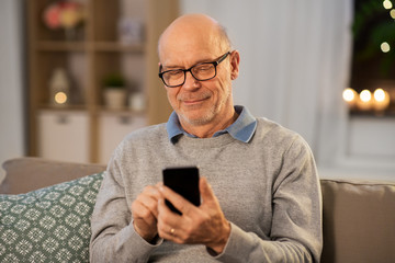 technology, people and communication concept - happy smiling bald senior man texting on smartphone at home in evening
