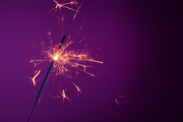 Shiny bright burning bengal fire party sparkler on purple background with copy-space