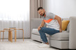 © New Africa - Man suffering from hemorrhoid on sofa at home