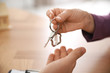 © New Africa - Real estate agent giving key with trinket to client in office, closeup