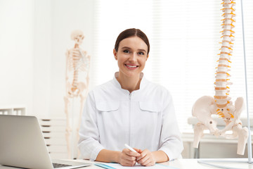 Poster - Female orthopedist with laptop near human spine model in office