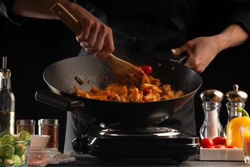 Cooking, the chef cooks pasta with sauce and vegetables in a pan, or wok, against a background of vegetables .. cooking. Recipe book, cooking and gastronomy