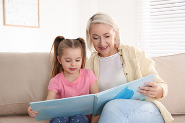 Poster - Mature woman with her little granddaughter reading book together at home