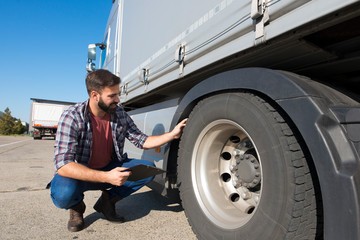 Wall Mural - Truck driver inspecting tires and checking depth of tire tread for safe ride. Controlling vehicle before transportation service.