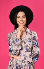 Wall Mural - Young woman wearing floral print dress and stylish hat on pink background