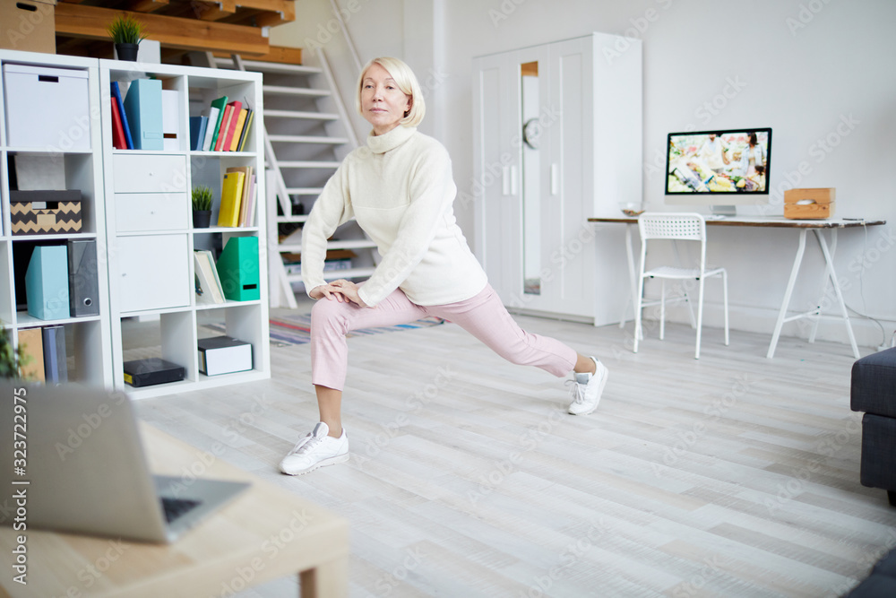 Full length portrait of active mature woman stretching legs during workout at home, copy space - obrazy, fototapety, plakaty 