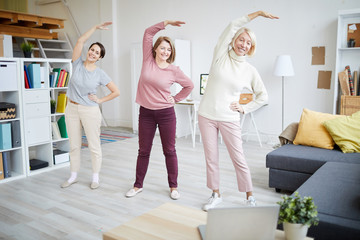 Wall Mural - Full length portrait of three adult women stretching during workout at home, copy space