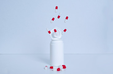 Wall Mural - Capsule bottle on surface and white background. The red and white capsules come out of the can. Concept of medicine.