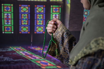 Wall Mural - Muslim woman praying for Allah muslim god at room near window. Hands of muslim woman on the carpet praying in traditional wearing clothes, Woman in Hijab, Carpet of Kaaba, Selective focus, toned