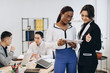 © anatoliycherkas - African and Caucasian White businesswomen using a tablet with interracial group of business men