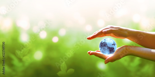 Card for World Earth Day. Blue planet crystal glass globe ball in human hand on blurred green background. Saving environment, save, protect clean planet and ecology, sustainable lifestyle concept.