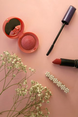 Blush, mascara, lipstick, beret and gypsophila flowers on pale pink background. Top view.