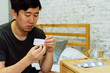 © twinsterphoto - Young Asian man feeling sick and taking pills while sitting on the bed at home with medicines tablets and drinking water on table. Healthcare and Medicine concept