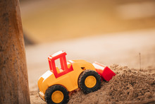 Yellow Digger With Shovel For Children Standing In The Sand Of A Playground For Kids.