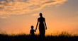 © kieferpix - Mother holding Childs hand walking through a field at sunset.