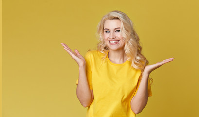 Wall Mural - Young happy woman shows hands up, spreads his hands to the sides. Above is an empty place for text and inscription on a yellow background.