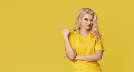 Wall Mural - Young happy woman shows hands up, spreads his hands to the sides. Above is an empty place for text and inscription on a yellow background.