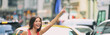 © Maridav - Hailing a taxi cab ride in New York City header. Asian woman with hand up for rideshare car in traffic panoramic banner.