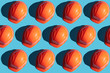 © Andrii - orange safety helmet rows on a blue background with hard shadows. looking from above.industrial pattern backdrop.