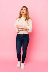 Young blonde caucasian woman standing over a pink background tired of a repetitive task.