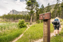 Man Hiking In The Mountains, Past Trail Head Sign, Near A Lake. Greenough Lake,  Montana, USA