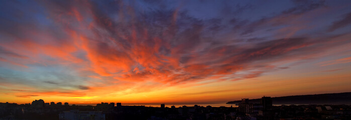 Wall Mural - panorama of dawn fire in the sky over a small seaside city. golden red clouds just before the sunris
