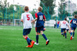 © Natali - Boys in white and blue sportswear plays  football on field, dribbles ball. Young soccer players with ball on green grass. Training, football, active lifestyle for kids concept