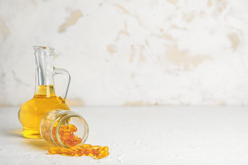 Jar with scattered pills and bottle of oil on white background