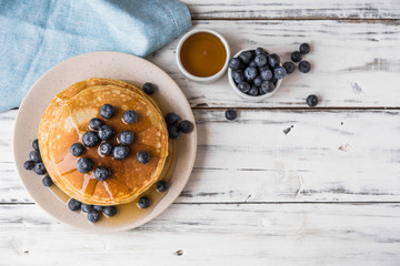 Close up of fluffy pancakes with maple syrup and blueberries against white wooden background