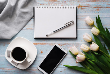 Wall Mural - Spring blanks of a freelancer's workplace with a bouquet of white tulips, a smartphone, an empty white bouquet and a Cup of coffee in his hands on wooden background