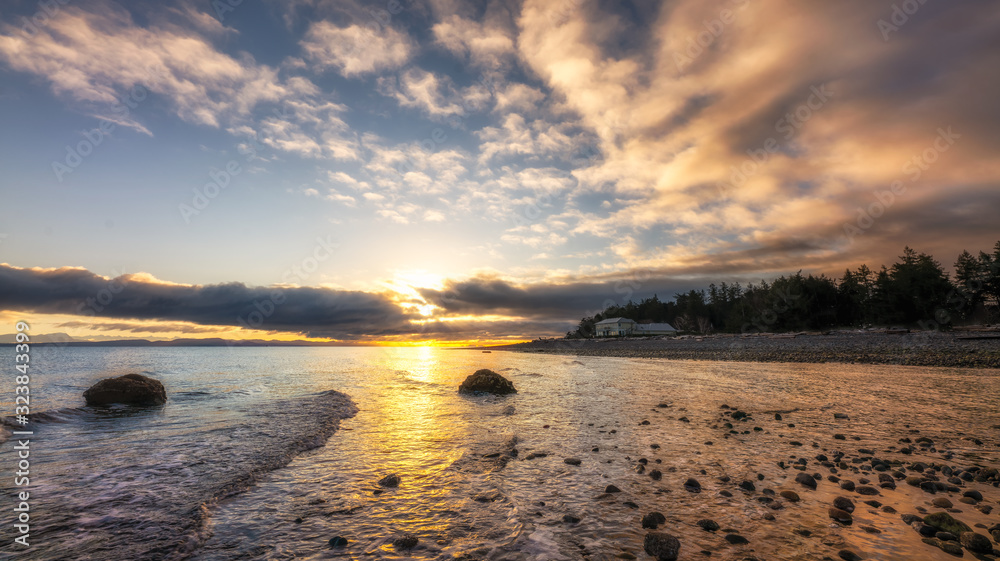 Beautiful sunrise under dramatic clouds along a shore with a lone house. - obrazy, fototapety, plakaty 