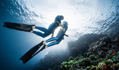 Two freedivers swim over the vivid coral reef in a tropical sea during their recreational freedive session