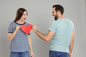 Wall Mural - Couple tearing paper heart on light grey background. Relationship problems