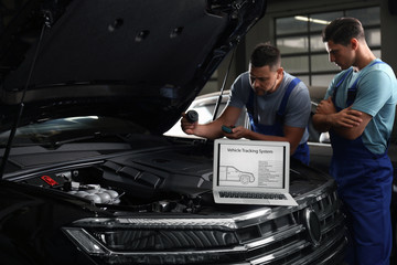 Wall Mural - Laptop with vehicle tracking system and blurred mechanics on background. Auto diagnostic