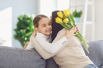 Happy mothers day. Daughter congratulates hugs his mother holds a bouquet of flowers in the room.