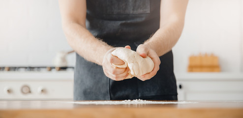 Banner Male baker prepares dough with hands for baking bread, wooden table white background