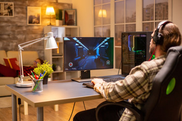 Wall Mural - back view of gamer male playing a shooter on his powerful pc computer late at night in the living ro