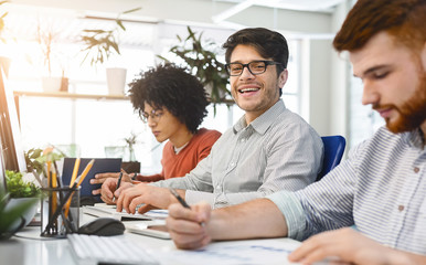 Poster - Smiling handsome man working in front of laptop with colleagues