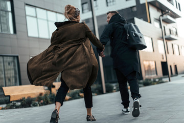 Back view of beautiful and young love couple holding hands and walking running on the road of urban city. Photo in motion