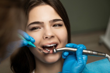 dentist in blue gloves filling the beautiful smiling woman patient's root canal using mirror under the medical lamp in clinic close up, healthcare concept