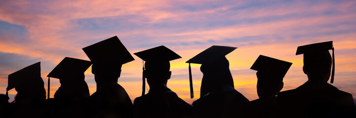 Wall Mural - Silhouettes of students with graduate caps in a row on panoramic sunset background. Graduation ceremony at university web banner, class of 2024