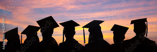 Cuadros en Lienzo Silhouettes of students with graduate caps in a row on sunset background