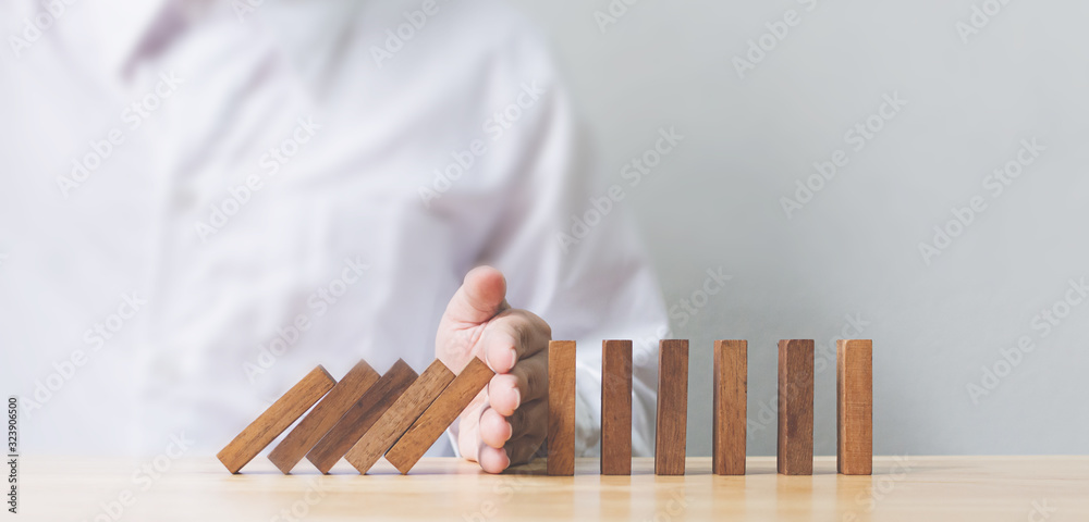 Hand stopping wooden domino business crisis effect or risk protection concept - obrazy, fototapety, plakaty 